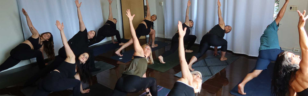 A class side-bending with one arm overhead in a dimly lit room with a dark wood floor